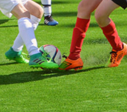 Fotboll_Springande ben med fotbollsskor och en fotboll på gräsmatta