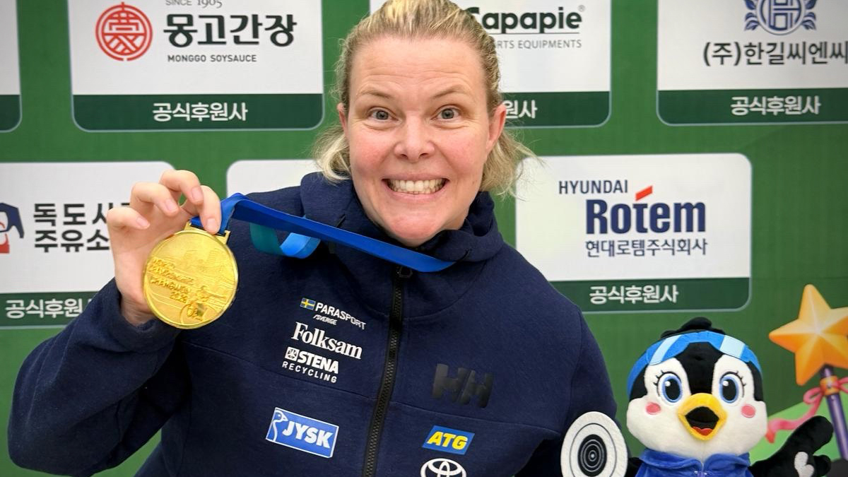 Anna Benson håller upp sin guldmedalj, tittar in i kameran och ler.